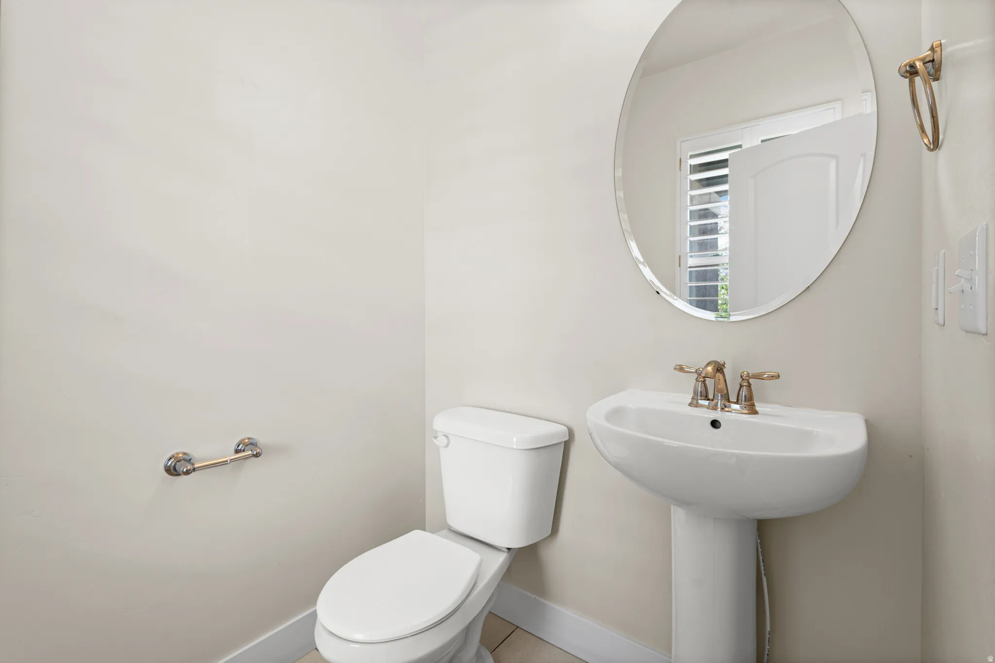 Pedestal sink with brass-finish faucet, accompanied by an oval frameless mirror