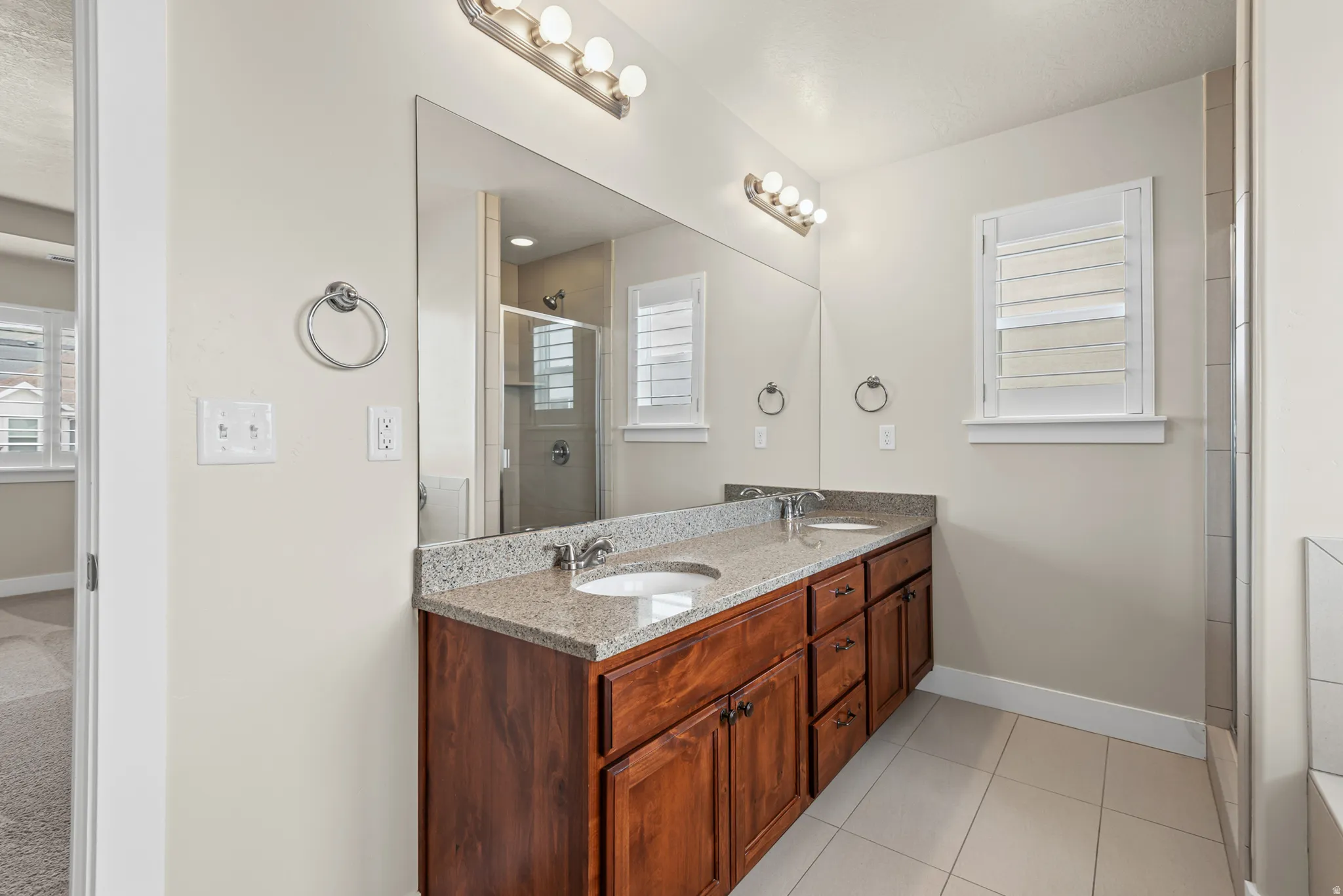 Spacious bathroom featuring a double vanity with wood-finish cabinetry, granite-style countertop, and dual undermount sinks