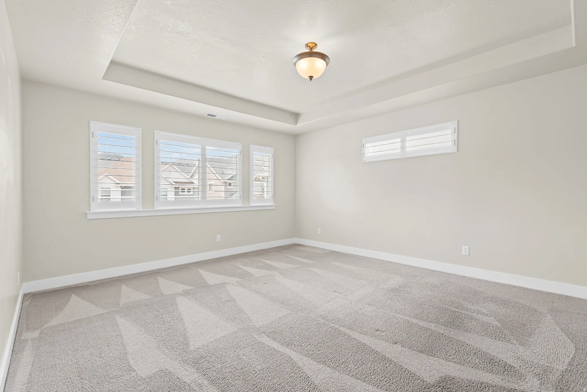 Spacious room featuring a tray ceiling with recessed lighting, light gray walls, and patterned carpet flooring