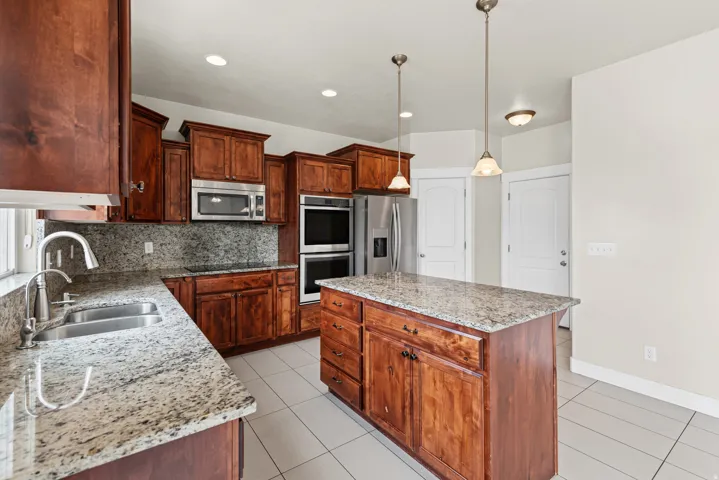 Spacious kitchen featuring rich wood cabinetry, granite countertops, stainless steel appliances, a center island with pendant lighting, and tile flooring