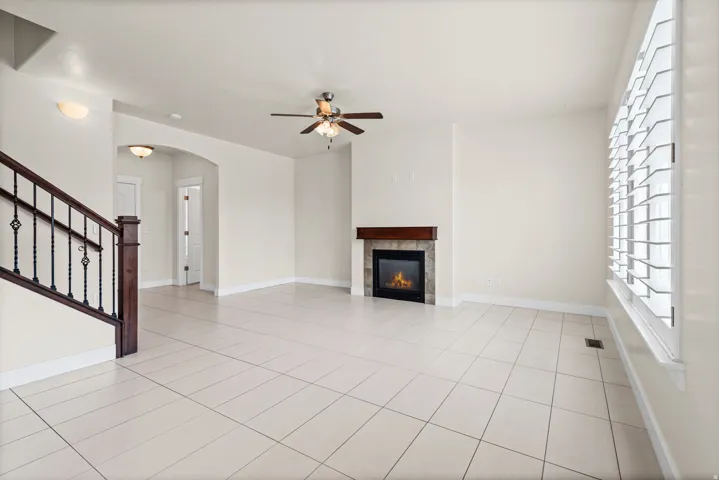 Spacious living area featuring light-toned tile flooring, a fireplace with a stone surround and wood mantel, and a ceiling fan