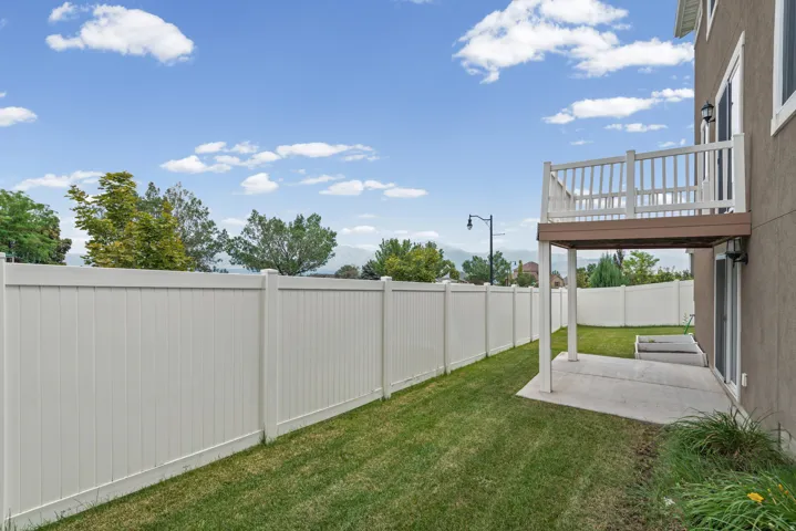 Fenced backyard with a concrete patio, elevated deck, and mature landscaping