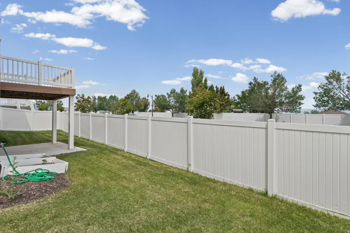 Expansive backyard featuring a manicured lawn, full privacy fencing, a concrete patio, and an elevated wood-finish deck with white railings