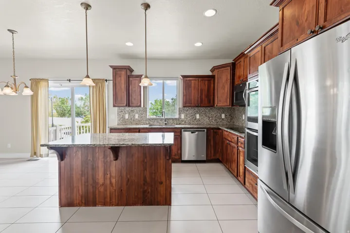 Kitchen featuring a central island with a granite countertop, extensive wood cabinetry, stainless steel appliances, and white tile flooring