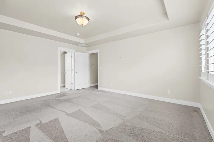 Spacious room featuring a tray ceiling, contemporary ceiling light fixture, white plantation shutters, and light-toned walls