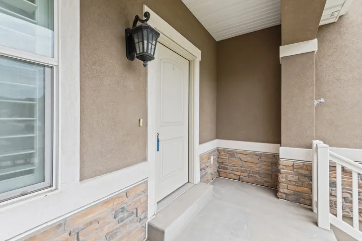 Inviting front porch featuring a white panel door, stucco siding, and a stone veneer base