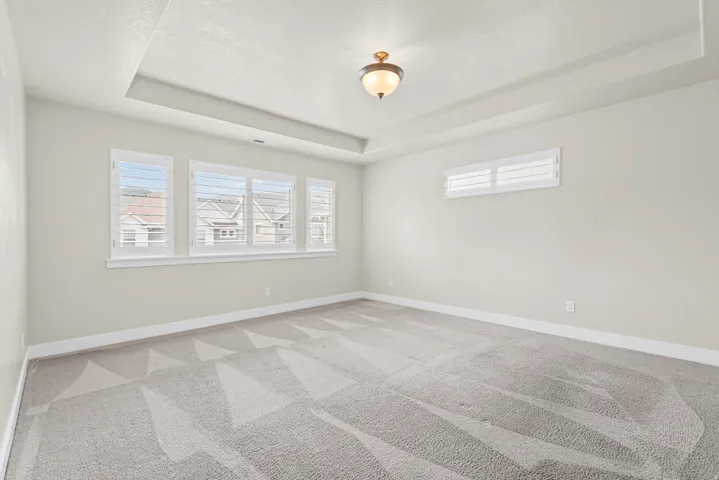 Spacious room featuring a tray ceiling with recessed lighting, light gray walls, and patterned carpet flooring