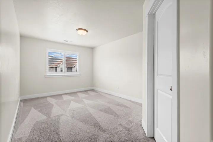 Neutral-toned room featuring a window with plantation shutters, a patterned gray carpet, white baseboards, and a flush-mount ceiling light