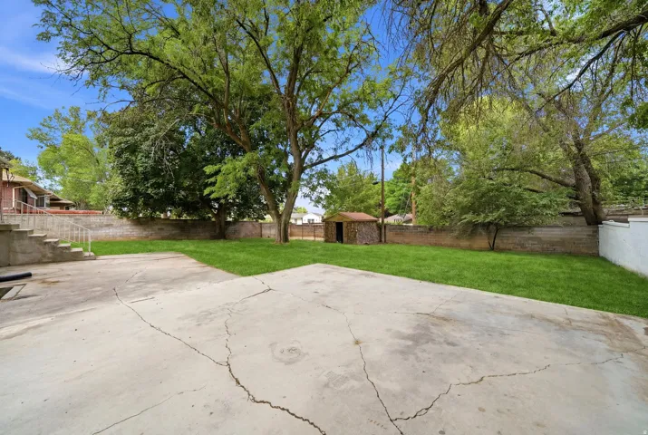 Expansive backyard featuring a concrete patio, a manicured lawn, and mature trees