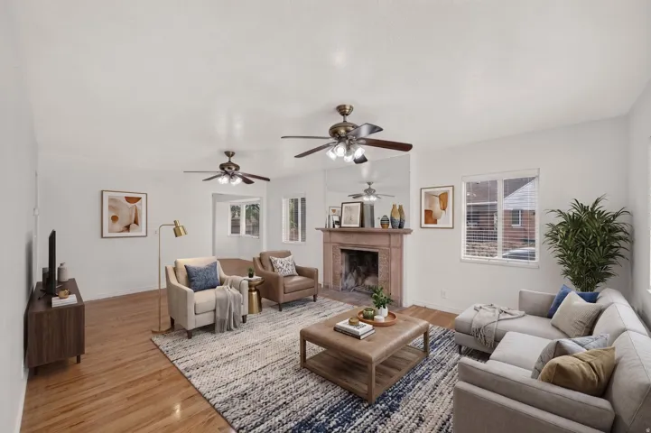 Spacious living area featuring hardwood flooring, a decorative fireplace with a substantial mantel, multiple windows, and two ceiling fans