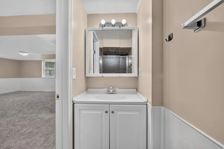 Bathroom vanity with white cabinetry, integrated sink, and an overhead medicine cabinet featuring a three-bulb light fixture
