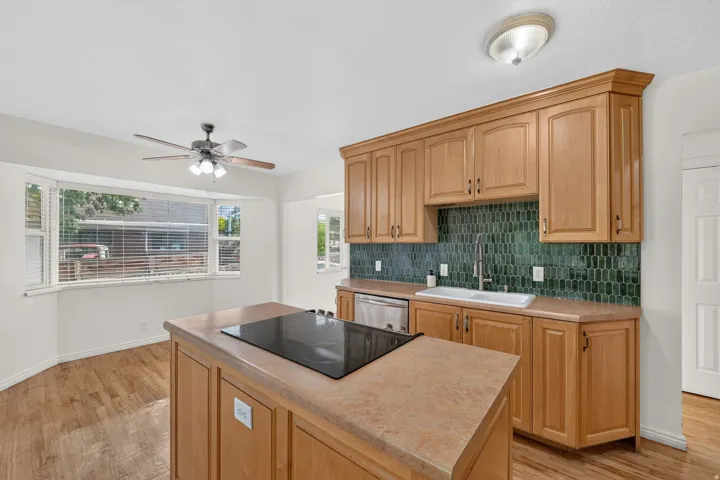 Kitchen featuring wood-finish cabinetry, a green geometric tile backsplash, and a central island with an integrated cooktop