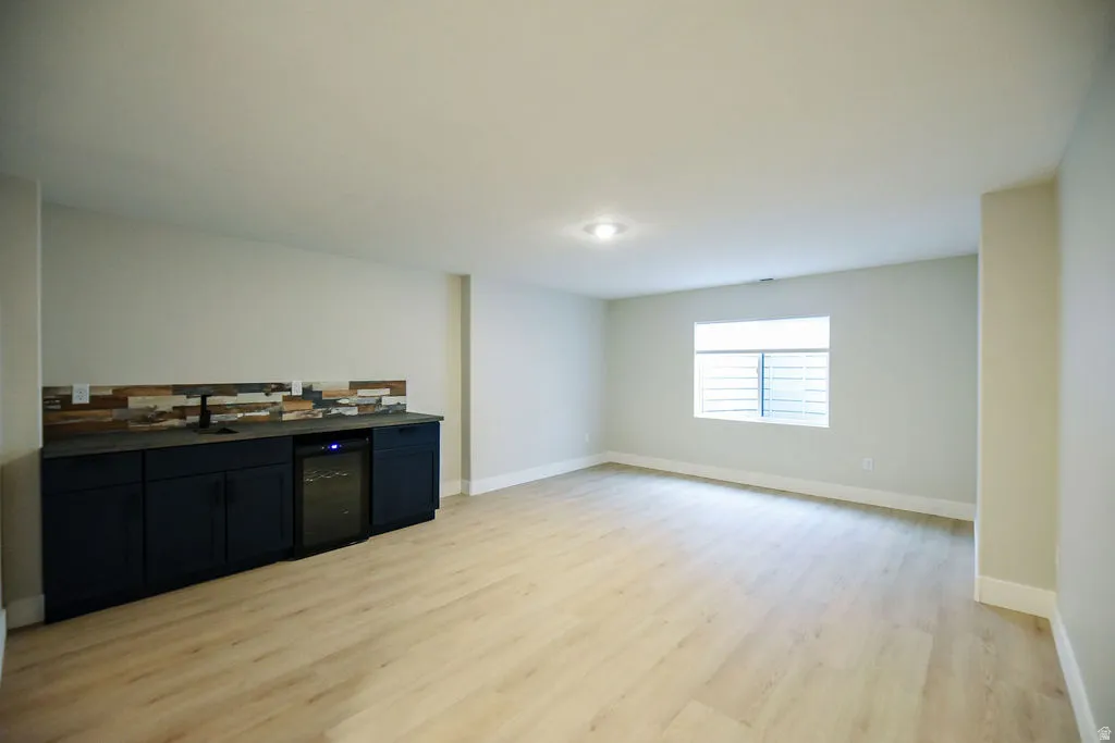 Spacious room featuring wood-finish flooring, a built-in wet bar with dark cabinetry, integrated beverage cooler, and a multi-tone tile backsplash