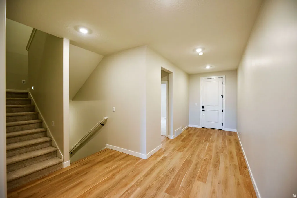 Entryway featuring wood-finish flooring, a white paneled door, recessed lighting, and a carpeted staircase with a handrail