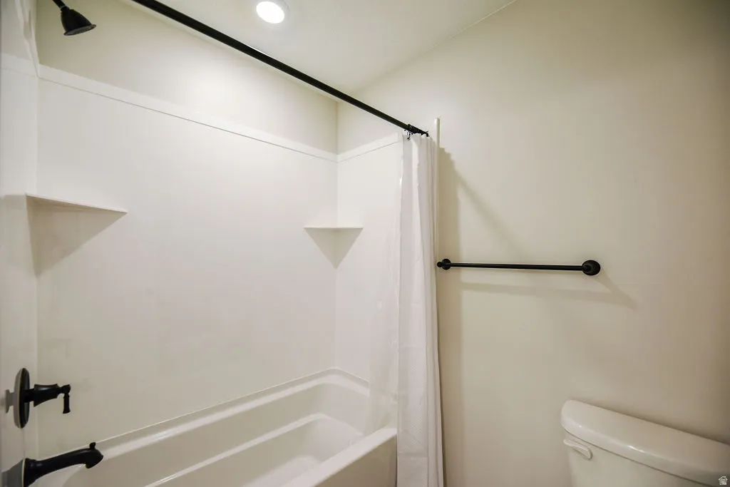 White tub and shower combination featuring integrated corner shelves, a matte black shower head, and coordinating matte black tub faucet and hardware
