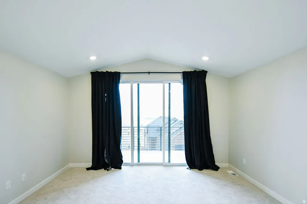 Spacious room featuring a vaulted ceiling with recessed lighting, light-colored carpeting, and a glass sliding door leading to an outdoor area
