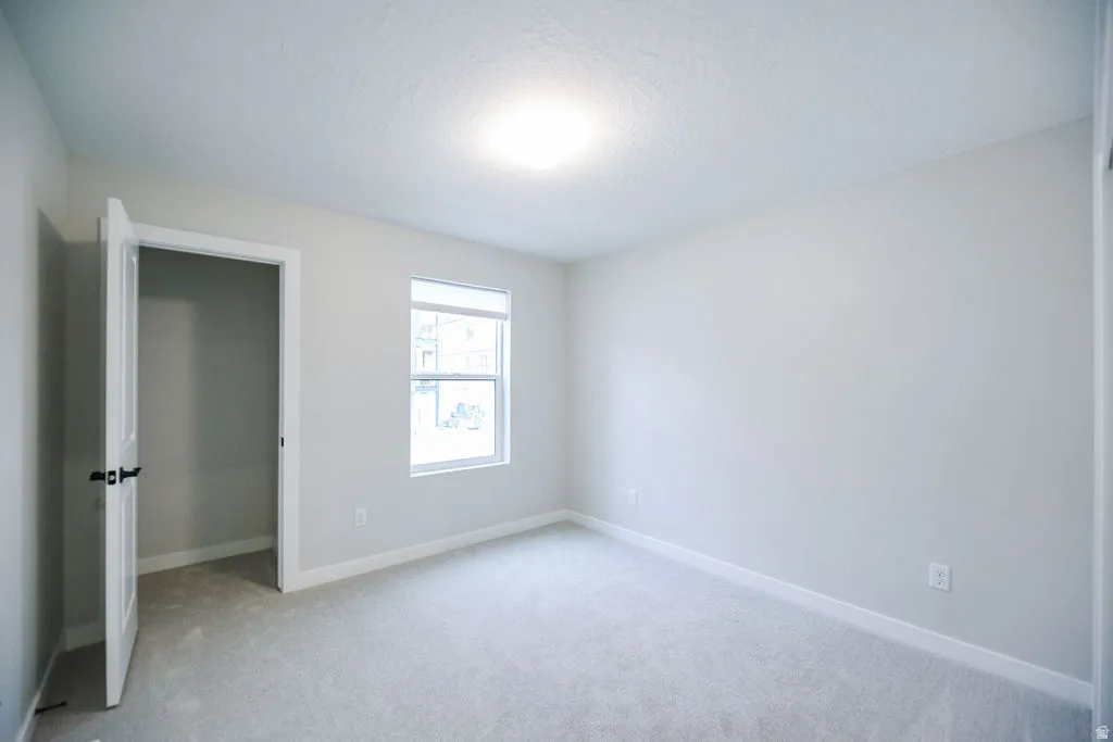 Carpeted room featuring a white interior door with black hardware, a single rectangular window, light gray wall paint, and white baseboards