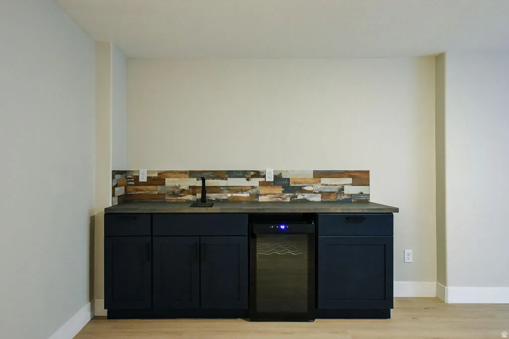 Built-in wet bar featuring dark cabinetry, a countertop sink with a matte black faucet, a textured wood backsplash, and an integrated beverage refrigerator
