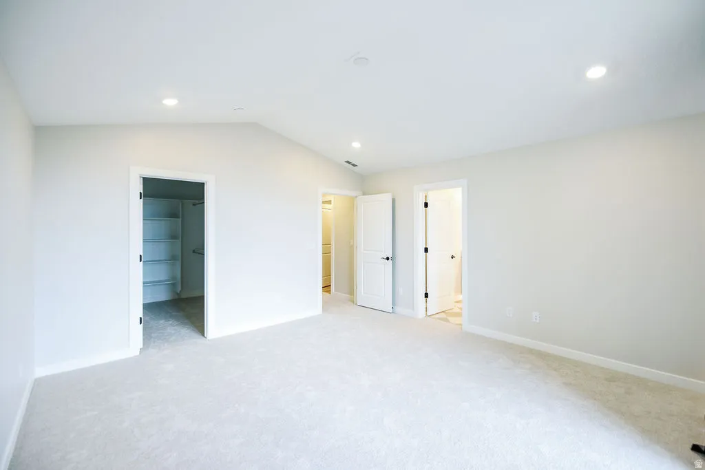 Spacious room featuring vaulted ceilings, recessed lighting, neutral wall tones, plush carpeting, and built-in closet shelving