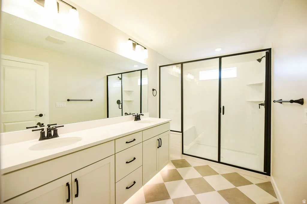 Spacious bathroom featuring a double vanity with stone countertops, a large frameless mirror, and dual lighting fixtures