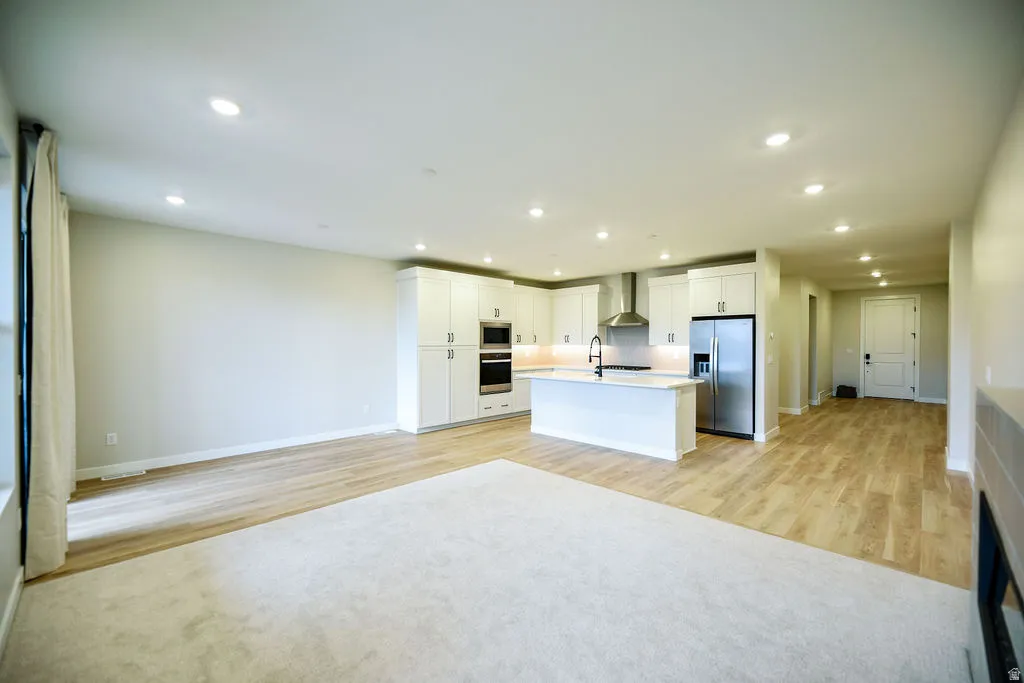 Open-concept living area featuring a modern kitchen with white cabinetry, stainless steel appliances, a center island with sink, recessed lighting, and wood-finish flooring
