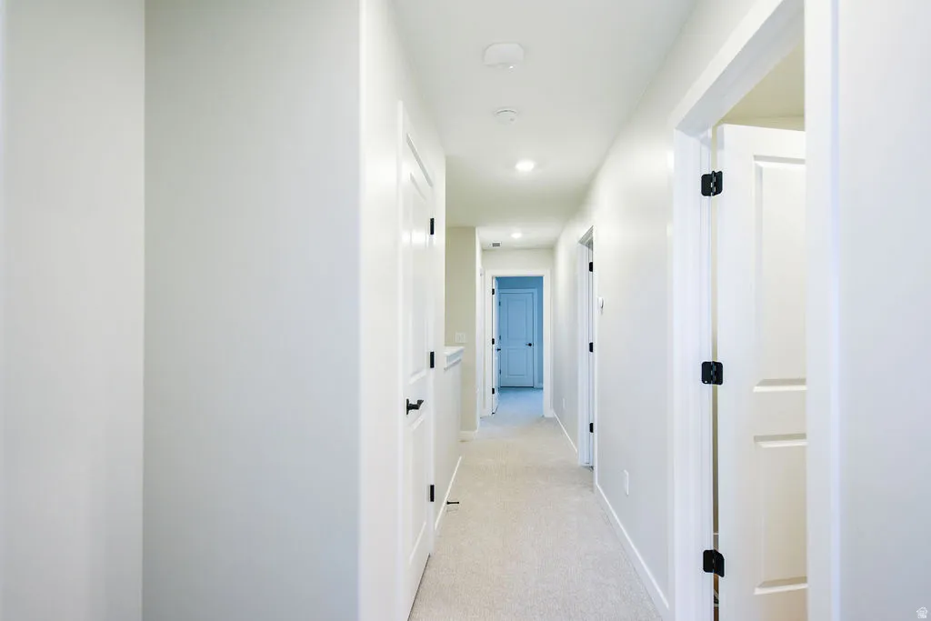 Bright hallway featuring recessed lighting, light-toned carpeting, white walls, and multiple paneled doors with matte black hardware