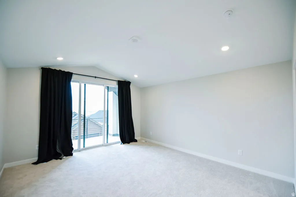 Spacious room with plush light-colored carpeting, a vaulted ceiling, and recessed lighting