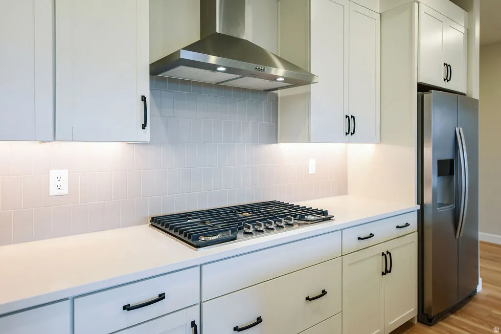 Modern kitchen featuring light cabinetry, a gas cooktop, stainless steel range hood, stone countertops, and a subway tile backsplash