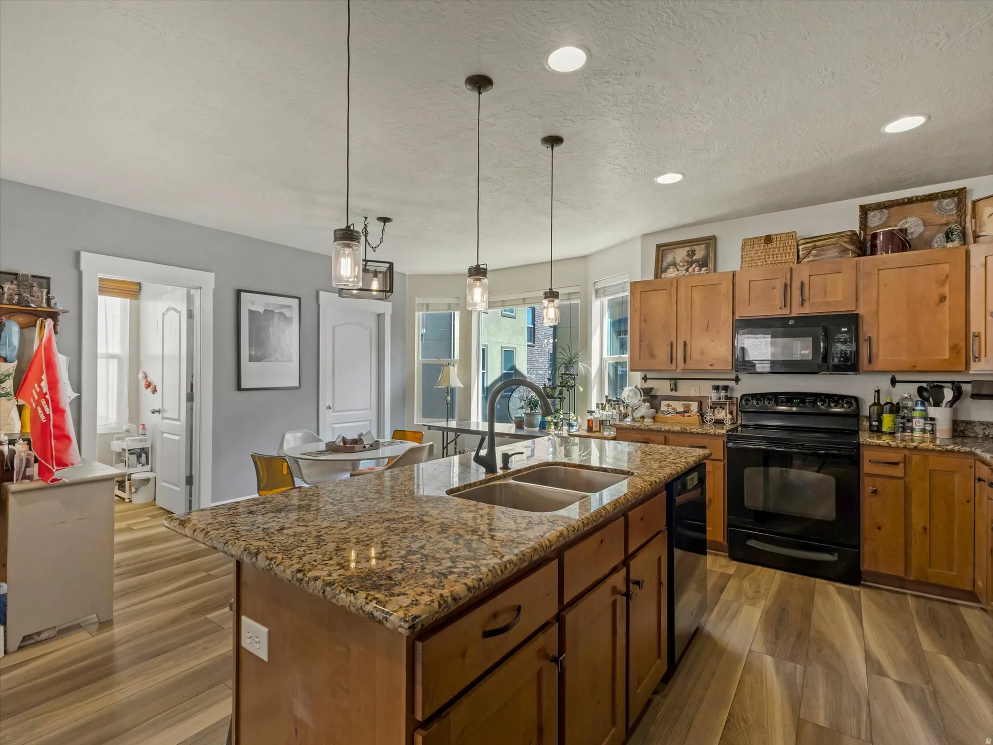 Kitchen featuring wood-finish flooring, an oversized island with a double basin sink, recessed lighting, and pendant light fixtures