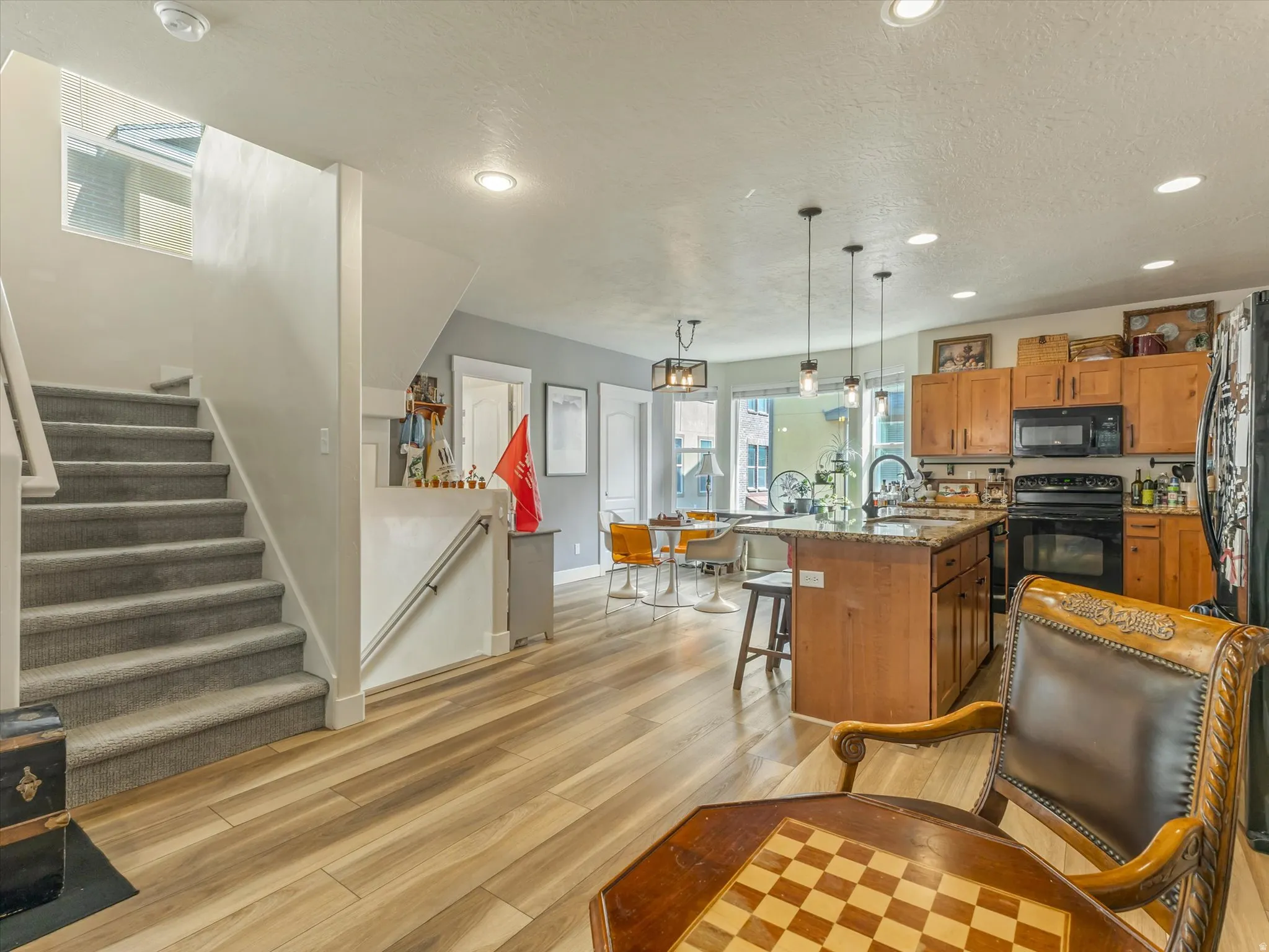 Spacious open-concept living area featuring wood-finish flooring, a kitchen island with stone countertop, and a full suite of black kitchen appliances