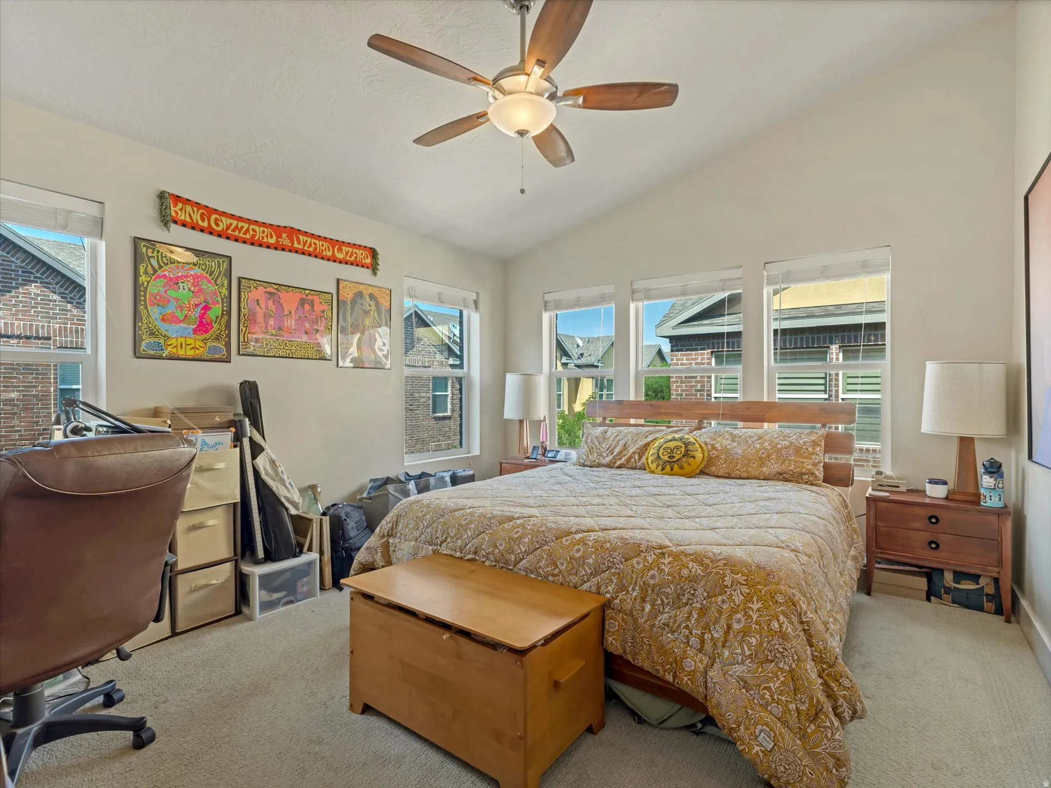 Carpeted room featuring a vaulted ceiling with a ceiling fan, multiple windows, and a built-in wooden headboard