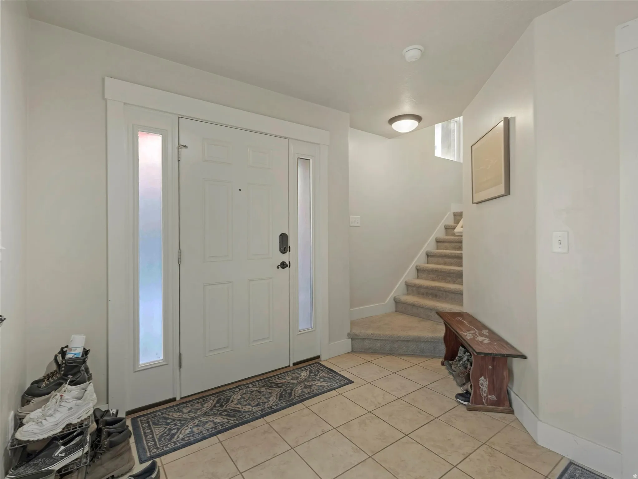 Entryway featuring a white paneled door with sidelights, neutral tile flooring, and a carpeted staircase