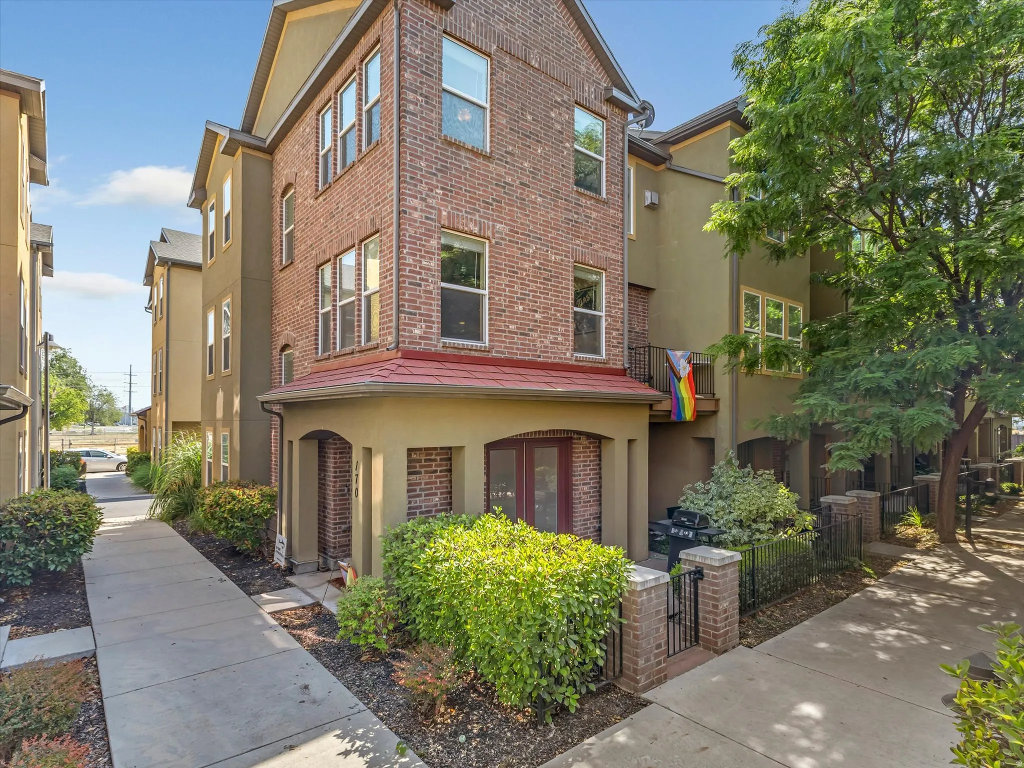 Three-story townhome featuring a brick and stucco exterior, arched entry, and a red tiled overhang