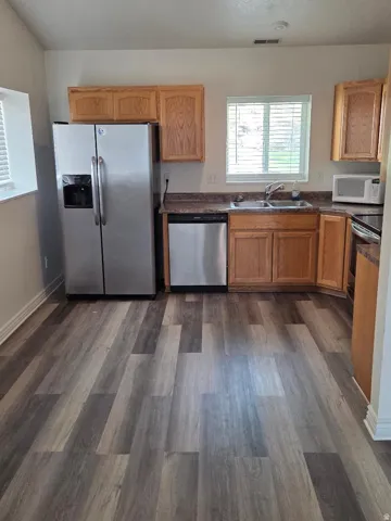Kitchen featuring wood-finish flooring, oak cabinetry, stainless steel refrigerator, stainless steel dishwasher, and a double basin sink