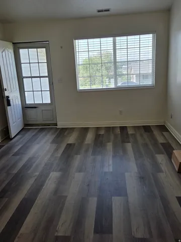 Spacious room featuring wood-finish flooring, a large window with blinds, and a paneled entry door