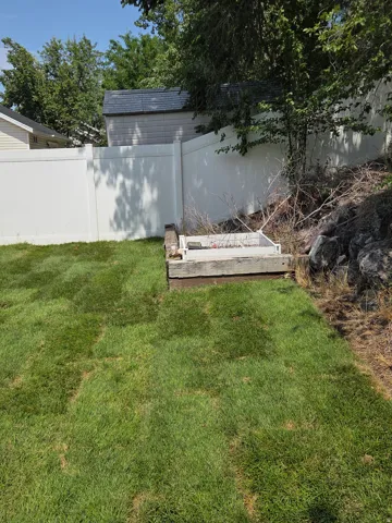 Expansive rear yard featuring green lawn, white privacy fencing, and a built-in planter box with wood-finish trim