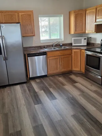 Kitchen featuring wood-finish flooring, stainless steel appliances, wood cabinetry, a double basin sink, and a window with blinds