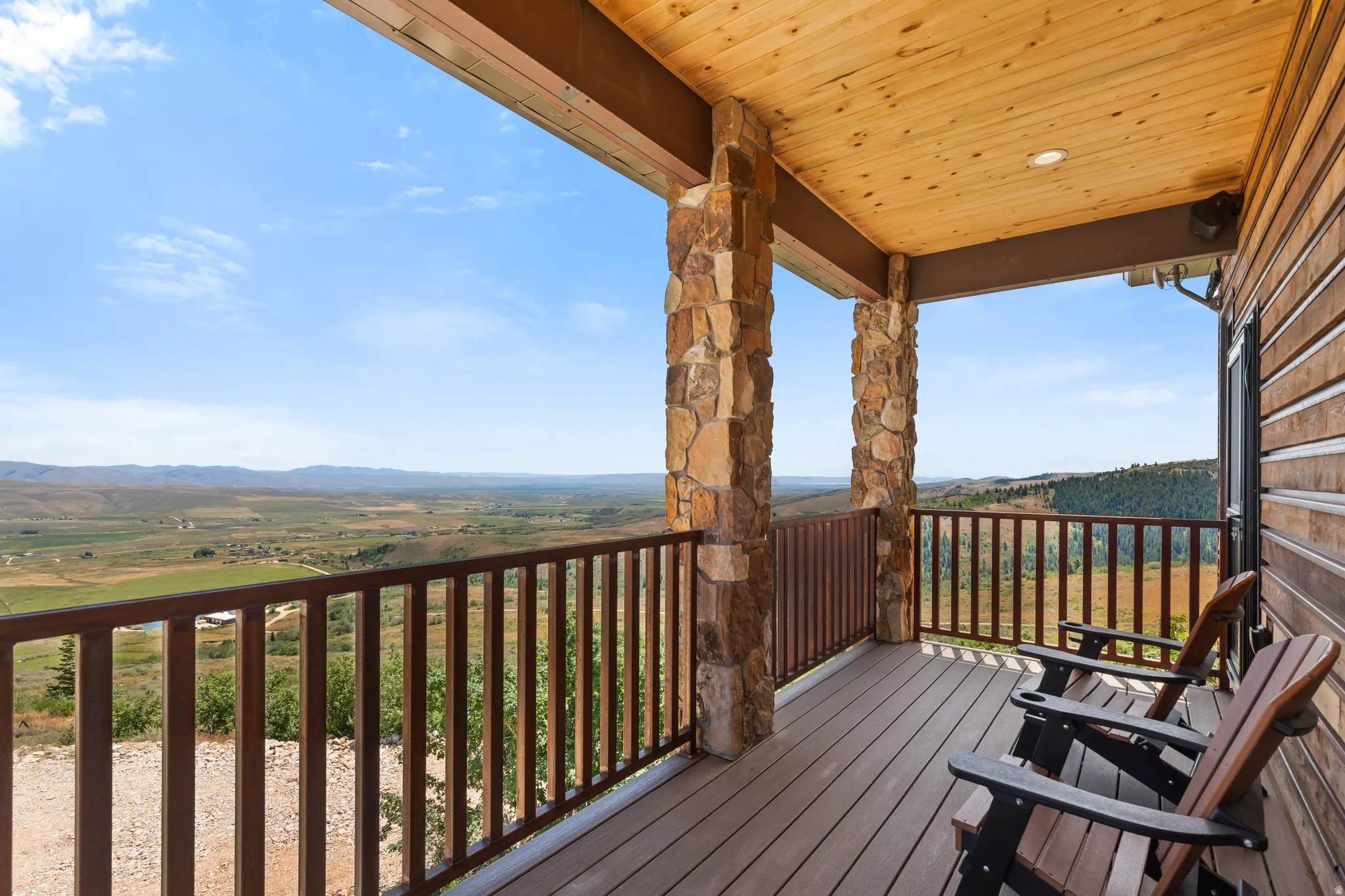 Covered deck featuring stone-clad pillars, wood-finish ceiling, and durable composite decking, overlooking expansive mountain and valley scenery