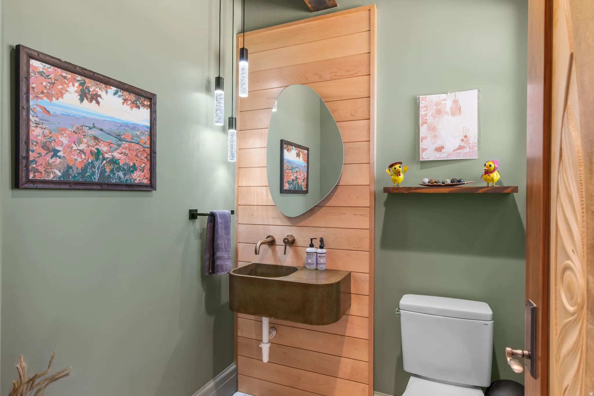Powder room featuring a wall-mounted basin sink with wall-mounted bronze faucet, a decorative mirror, and three pendant light fixtures