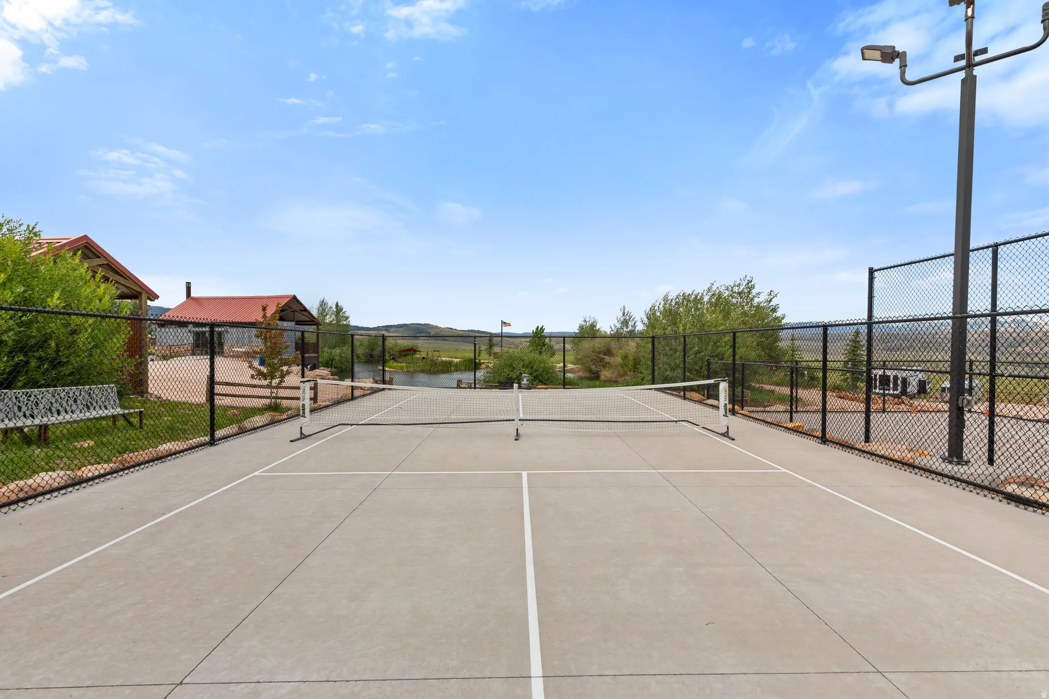 Hard surface court with white line markings, black chain-link fencing, and integrated sports lighting