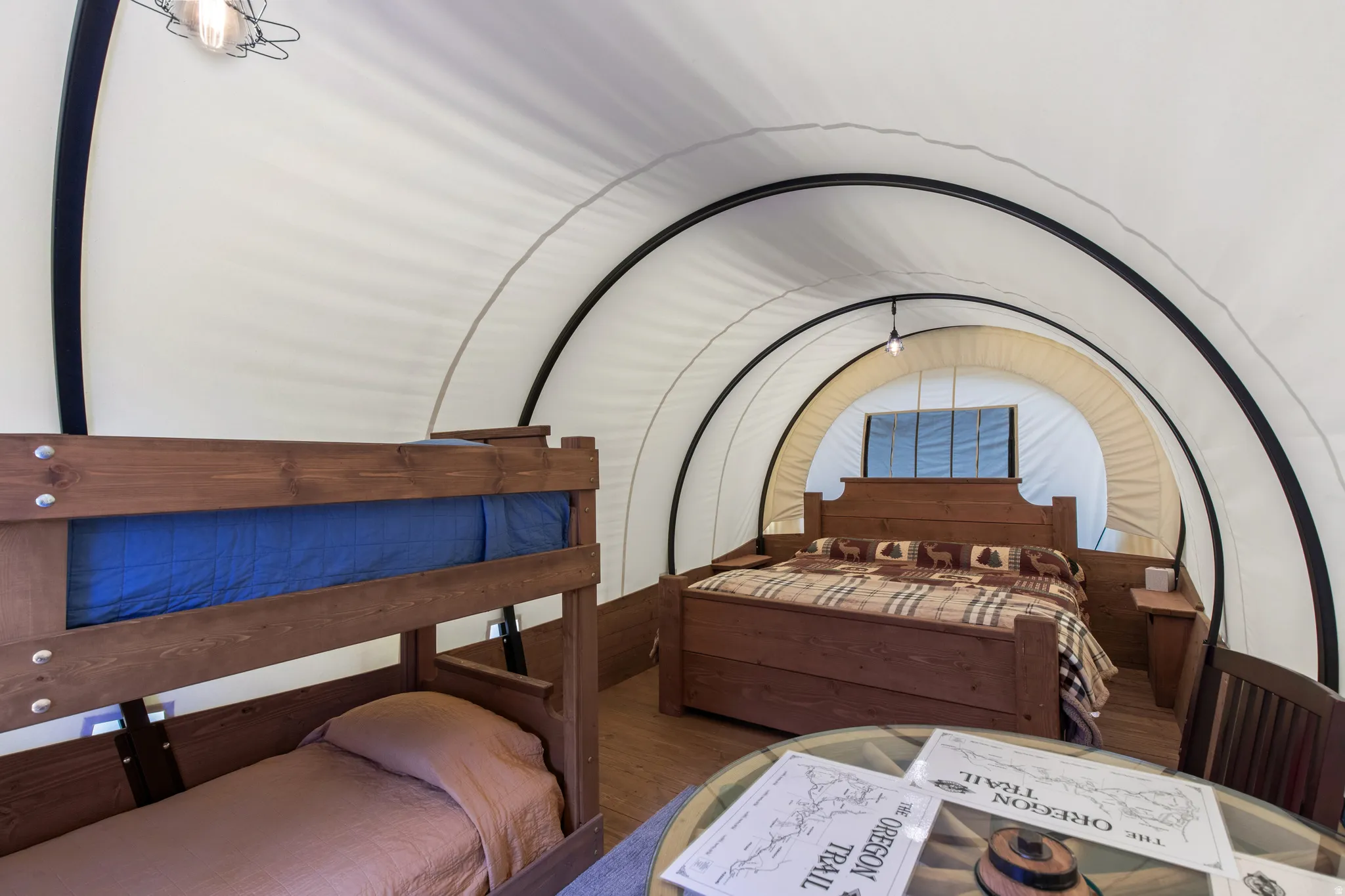 Interior space featuring wood-finish flooring, a full-size bed with a wood headboard, a bunk bed with a wood frame, a round glass-top table, and a central overhead light fixture