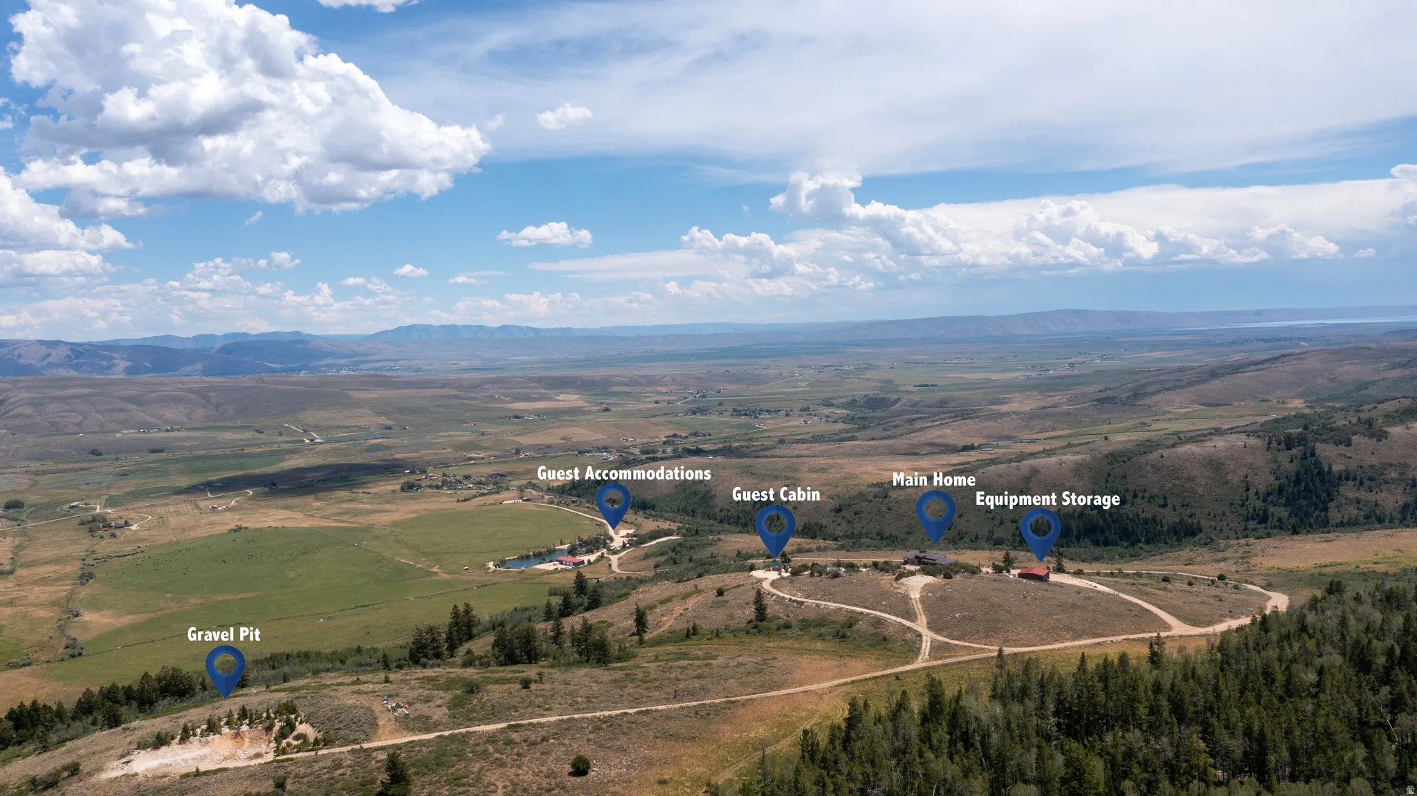 Aerial perspective showcasing multiple structures including a main home, guest cabin, guest accommodations, and equipment storage within a expansive landscape
