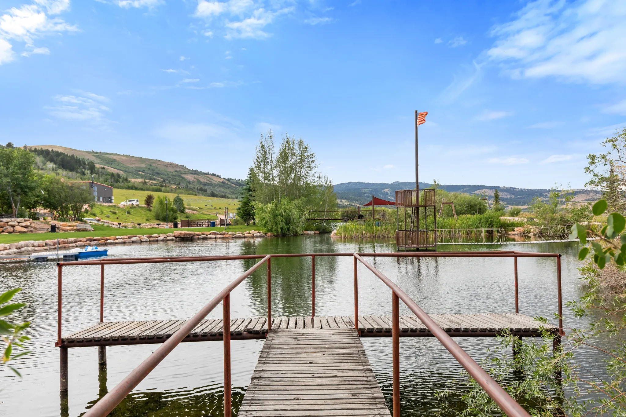 Wood dock extending over a pond, featuring a rustic metal railing and a wooden platform