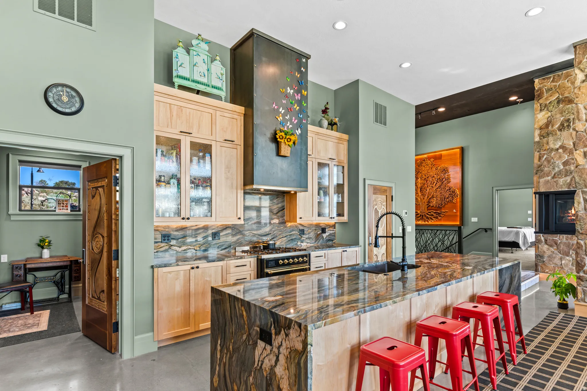Open-concept kitchen with a large island featuring a stone countertop, light wood cabinetry, a built-in range, and a decorative range hood