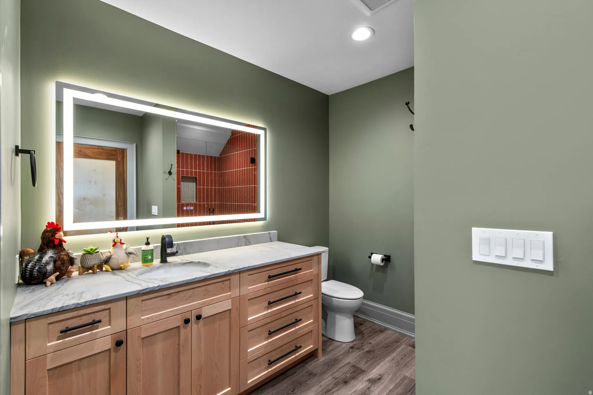 Bathroom featuring a light wood-finish vanity with ample storage, a light stone countertop, and a contemporary illuminated mirror