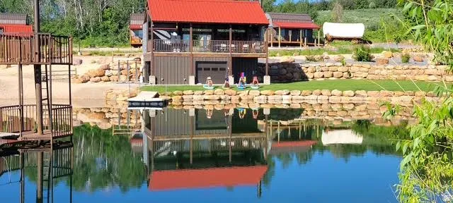 Waterfront property featuring a two-story structure with a red metal roof, a second-story balcony, and a ground-level garage door