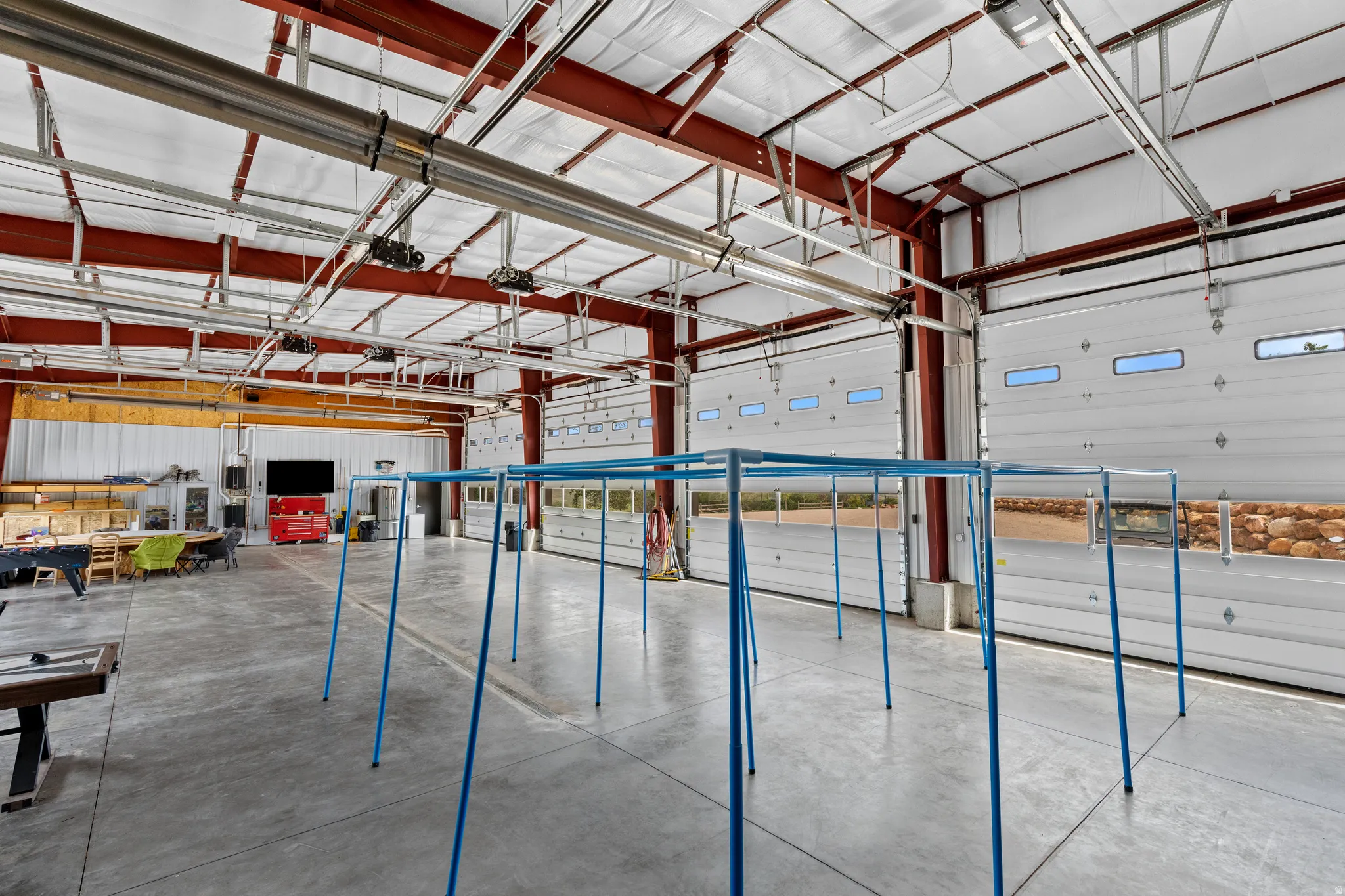 Expansive commercial bay featuring a polished concrete floor, red I-beam construction, and multiple overhead doors with integrated windows