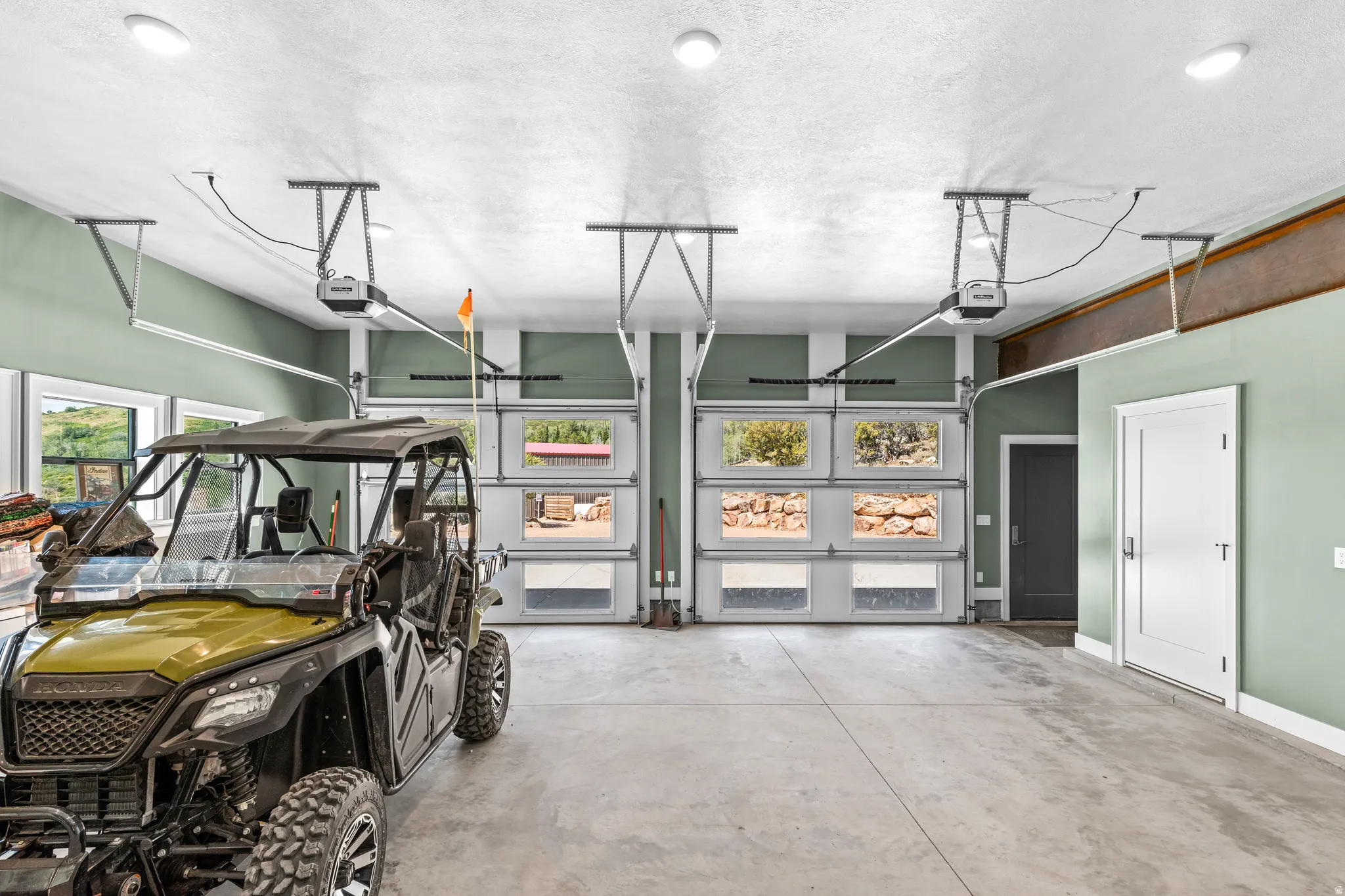 Spacious garage featuring a concrete floor, two overhead garage doors with frosted and clear glass panels, multiple recessed ceiling lights, and two interior doors