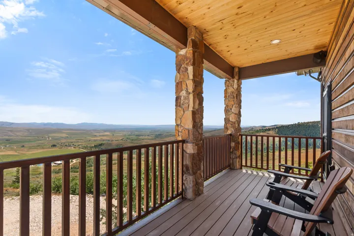 Covered deck featuring stone-clad pillars, wood-finish ceiling, and durable composite decking, overlooking expansive mountain and valley scenery