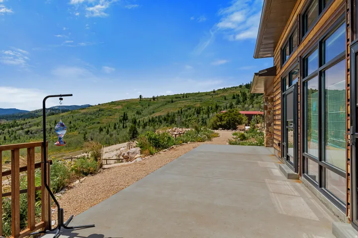 Expansive concrete patio with mountain views, featuring full-height windows, a wood-sided exterior, and a gravel walkway